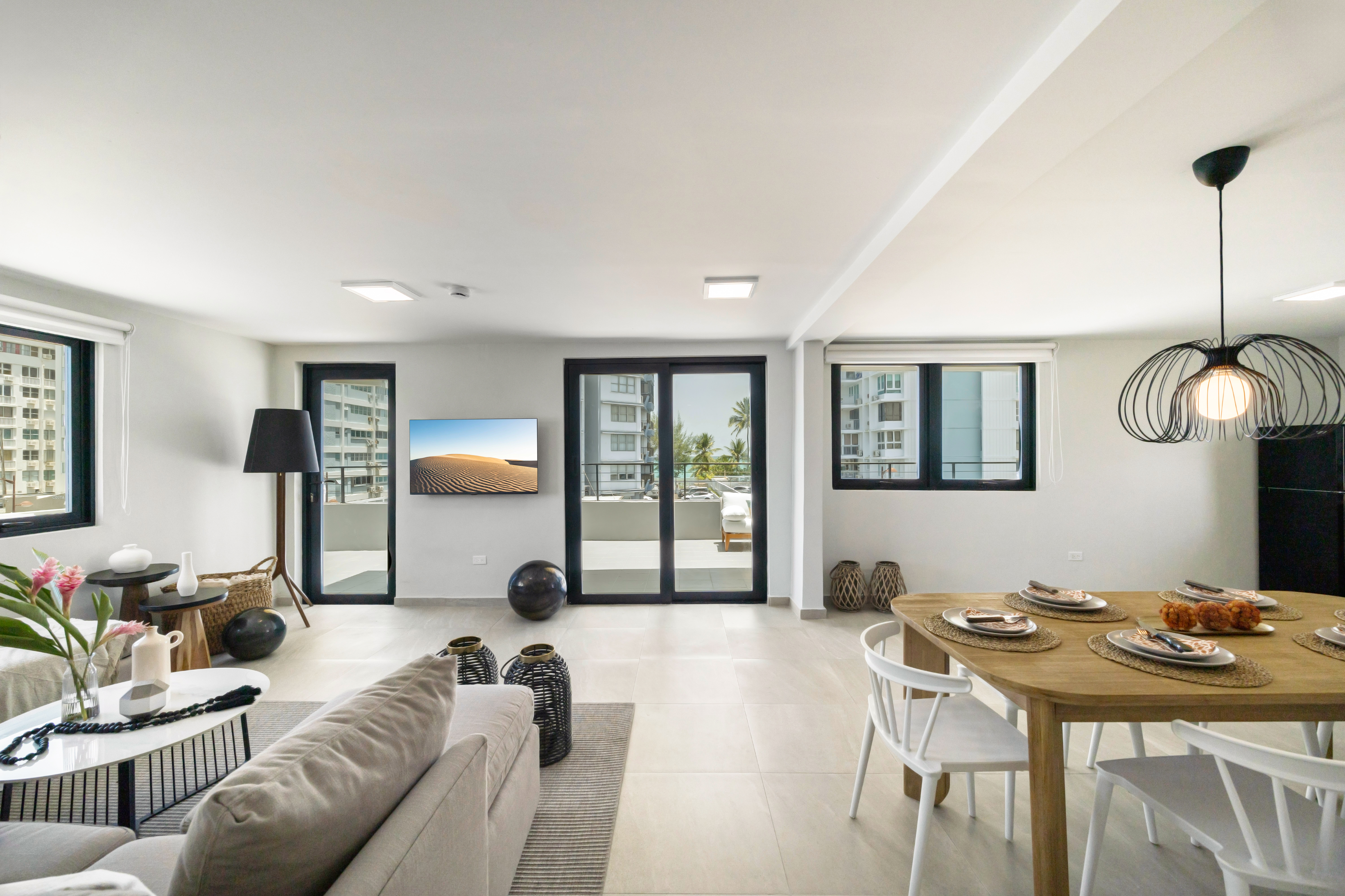 A modern and spacious living area featuring a cozy sofa, dining table, and stylish decor. Large windows provide natural light and reveal an oceanfront view.